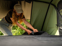 Woman adjusting the TentBox Lite XL Mattress Topper inside the rooftop tent – easy setup process