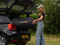 Woman loading packed TentBox Lite XL Mattress Topper into vehicle boot – compact and transportable