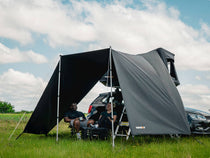 Two people sitting under the TentBox GO Tunnel Awning in a grassy field.